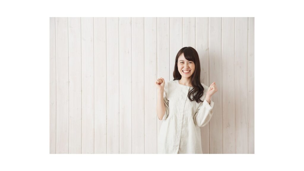 両手を握りしめて笑顔を見せる女性。不要な物を手放し、新しい運気を迎え入れる喜びを表現している。