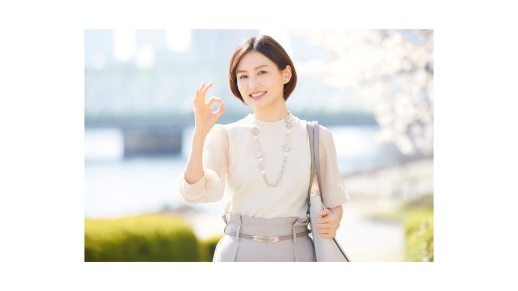 「屋外で笑顔を見せながらOKサインをする女性。達成感と満足感を表している。」