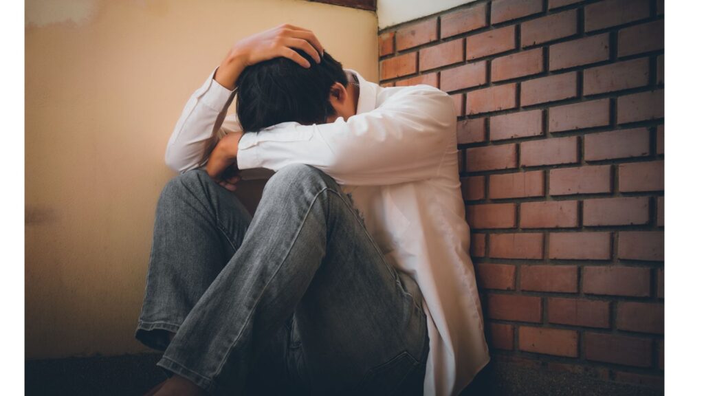 うなだれて膝を抱える男性。湿気や部屋干しによる気の停滞がメンタルや人間関係に影響しているイメージ。