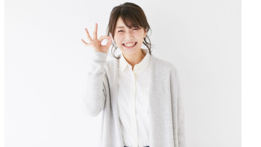 OKサインを出しながら笑顔を見せる女性。白い背景と明るい表情が、清々しい朝のイメージを演出している。